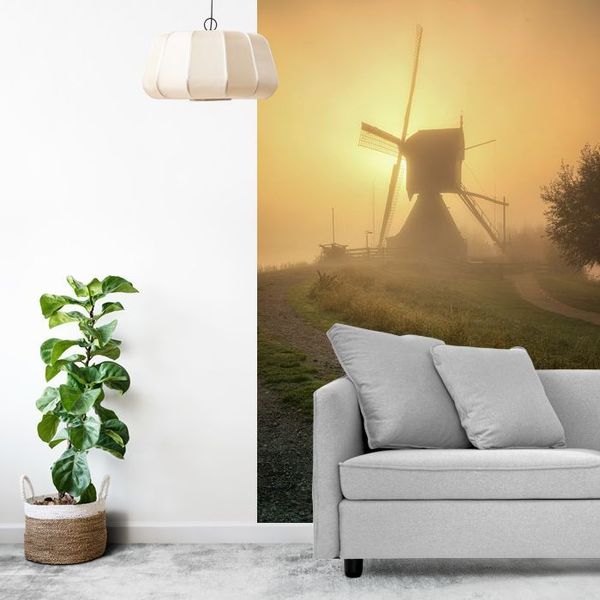 Wipmolen in Kinderdijk, de ochtendzon breekt door de mist en kleurt de lucht warm geel.
